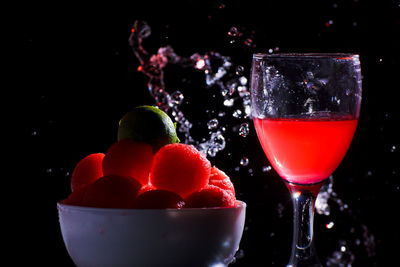 Close-up of fruits in bowl by red drink splashing against black background