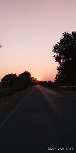 Road amidst silhouette trees against clear sky during sunset