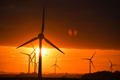 Silhouette wind turbines on land against sky during sunset