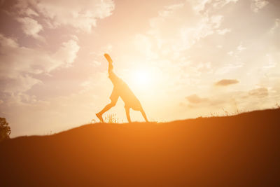 Side view of silhouette man with arms raised against sky during sunset