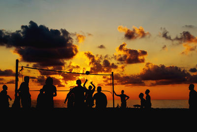 Silhouette people playing volleyball at beach against sky during sunset