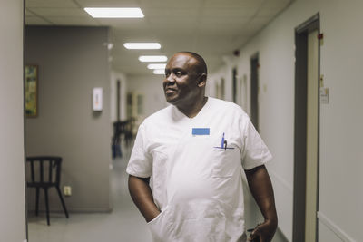 Mature male physician with hand in pocket walking in corridor at hospital