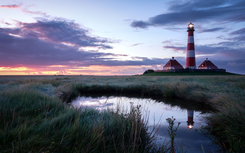 Lighthouse by lake against sky during sunset