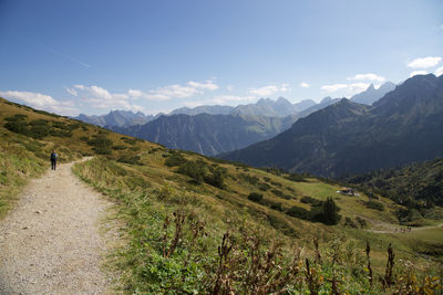 Rear view of man walking on the path by mountain against cloudy sky