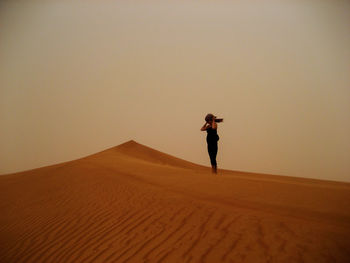 Woman standing on sandy desert against clear sky during sunset