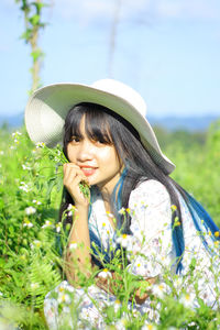 Portrait of young woman wearing hat sitting agains flowers
