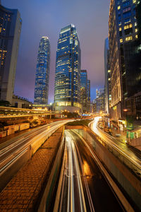 Light trails on road amidst buildings against sky at night