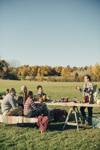 Instructor holding digital tablet while talking with farmers sitting at table on field