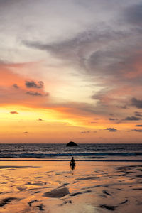 Silhouette person meditating at beach against sky during sunset