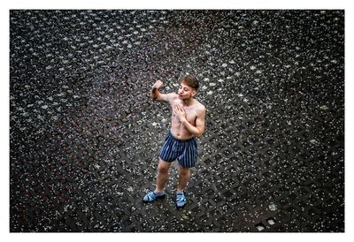 Shirtless young man flexing muscles while standing on street during winter