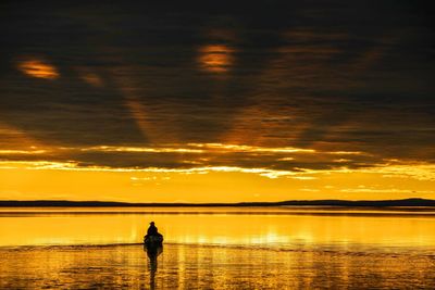 Silhouette person sailing canoe in river against cloudy sky during sunset