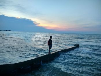 Man in sea against sky during sunset