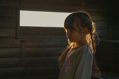 Side view of young girl standing against wall during sunset