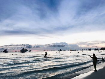 People at beach against sky during sunset