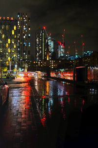 Illuminated buildings by wet street during rainy season at night