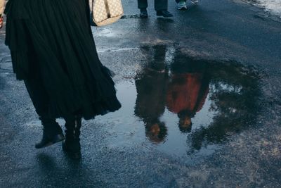 People reflecting in puddle on street