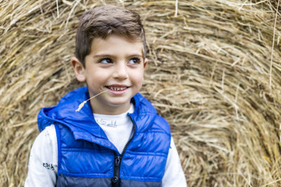 Cute boy standing against hay bale