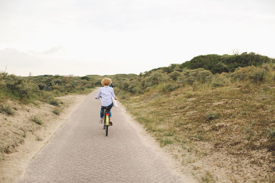 Full length rear view of woman riding bicycle on road against sky