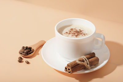 Cinnamon coffee cappuccino in white classic cup on beige background.