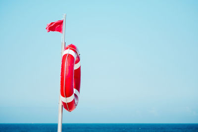 Low angle view of flag with inflatable ring against clear sky at beach