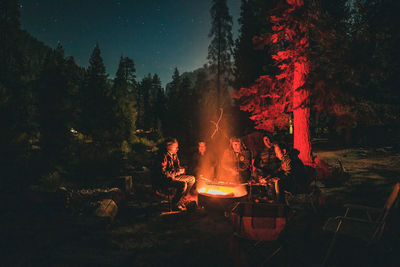 Men sitting by bonfire in forest at night