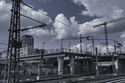 Low angle view of railroad tracks and cranes against sky