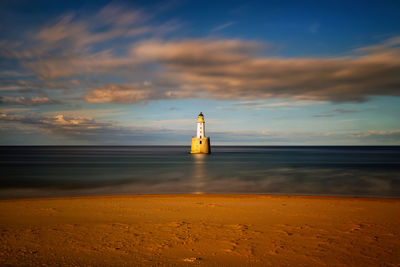 Lighthouse by sea against sky during sunset