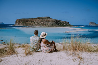 Rear view of woman sitting on beach against sky