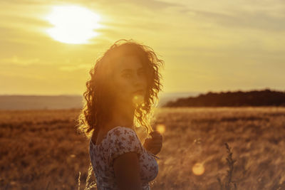 Young moroccan woman, with brown curly hair,  in wheat field, sunset and blinding the camera