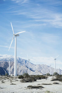 Wind turbines on farm by rocky mountain against sky