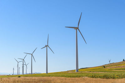 Windmills on field against clear blue sky