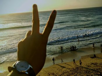 Close-up of hand by sea against sky