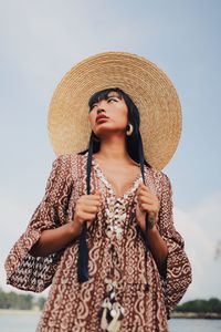  low angle view of young woman wearing hat standing at beach against sky