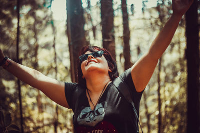 Midsection of woman with arms raised in forest