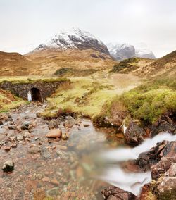 Stream and stony bridge in spring higland mountains in scotland. snowy mountains in heavy clouds