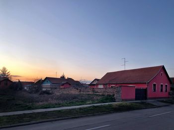 Road by buildings against sky during sunset