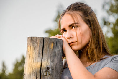 Young woman by wooden post against sky