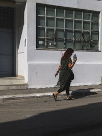 Young woman walking on street by building during sunny day