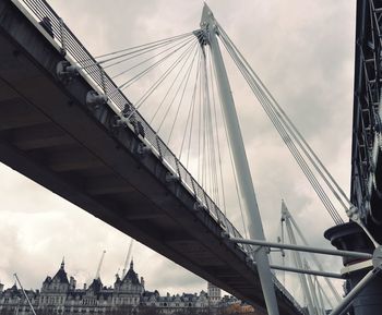 Low angle view of suspension bridge against cloudy sky