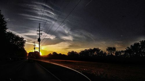 Silhouette of trees by road against sky during sunset