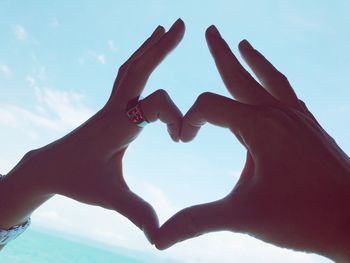 Close-up of woman hand holding heart shape against sky