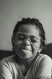 Close-up of cute girl wearing eyeglasses while sticking out tongue at home