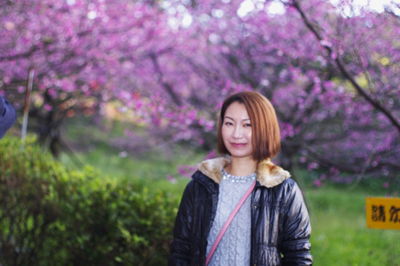Portrait of smiling woman standing on grassy field against cherry blossoms