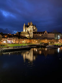 Illuminated buildings by lake against sky at night