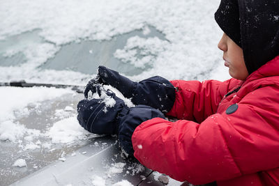 Boy plays with first snow lying on car.