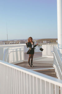 Woman standing on footbridge against clear sky