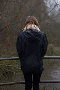 Rear view of woman standing by railing against bare trees