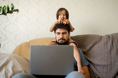 Young woman using laptop while sitting on sofa at home