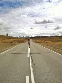 Woman standing on road passing through landscape against sky