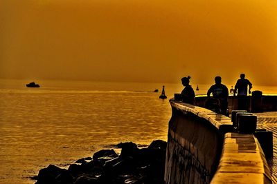 Silhouette people on sea against orange sky